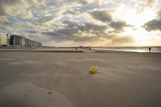 Sunlit beach with yellow buoy and people near shoreline at sunset. Blankenberge, West Flanders, Belgium