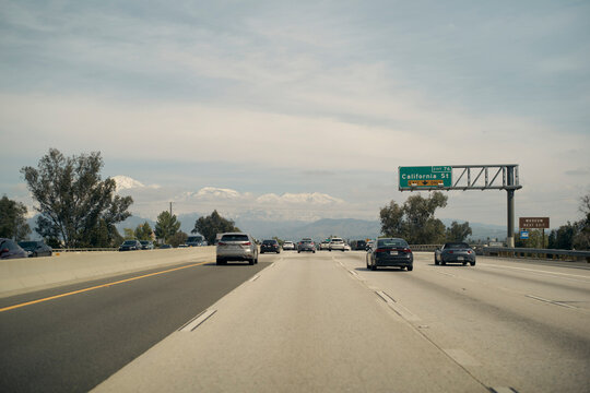 Busy highway with cars, trees, and mountains, under a cloudy sky with visible road signs. California, USA