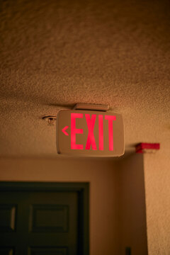 Red exit sign illuminated on a textured ceiling in a dimly lit hallway. California, USA
