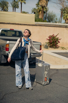 Young woman with luggage stands by a truck on a sunny street with palm trees in the background. California, USA