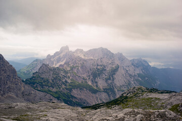 Rugged mountain range under cloudy sky with rocky foreground and lush greenery. Salzkammergut, Dachstein Mountains, Austria