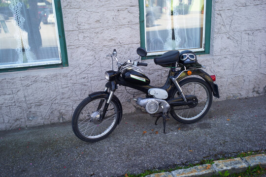 A vintage motorcycle parked on a gravel path beside a textured stone wall with two windows. Salzkammergut, Dachstein Mountains, Austria