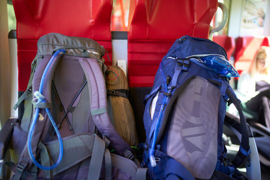Two large backpacks on a train seat, with a blurred passenger in the background. Salzkammergut, Dachstein Mountains, Austria