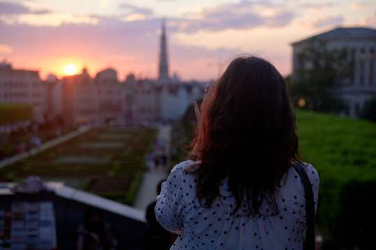 Woman viewing sunset over cityscape with silhouette of buildings and cloudy sky. Brussels, Belgium