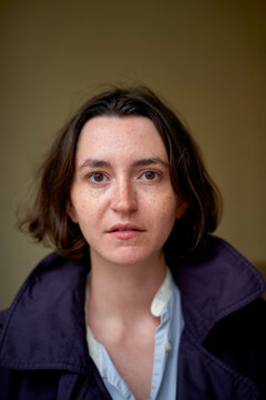 Woman in a dark coat and blue shirt looking directly at the camera indoors. Brussels, Belgium