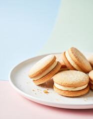 A plate of cream-filled cookies dusted with powdered sugar, set against a pastel background, inviting a sweet treat experience.
