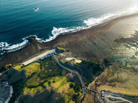 Aerial view of coastline with crashing waves, rocky shore, and lush green landscape. Lombok, Bukit Seger, Indonesia