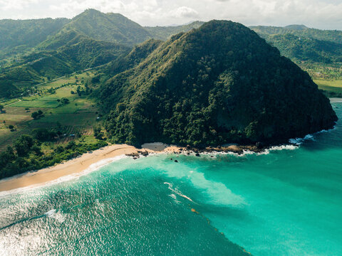 Aerial view of a lush green mountain and secluded beach with turquoise waves. Lombok, Resto Nine, Indonesia