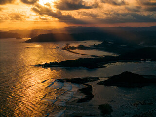 Dramatic sunset over a rugged coastline with golden rays lighting the sky and sea. Lombok, Gerupuk, Indonesia