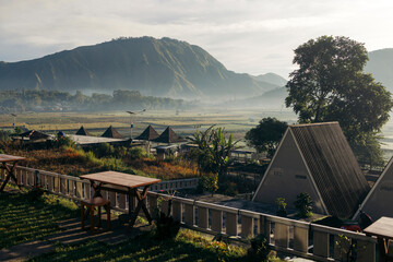 Mountain landscape with misty morning over a rural village and wooden picnic tables in foreground. Lombok, Senaru, Indonesia
