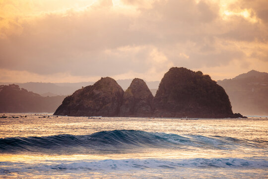 Rocky islands at sunset with waves rolling in, under a dramatic sky with clouds. Lombok, Mawi, Indonesia