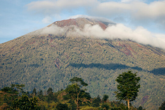 Majestic mountain with clouds and forested slopes under a blue sky. Lombok, Senaru, Indonesia