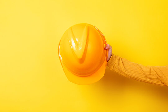 Hand holding a yellow construction helmet against a matching yellow background. Bright, minimal, and ideal for safety, construction, or industry concepts. - Powered by Adobe