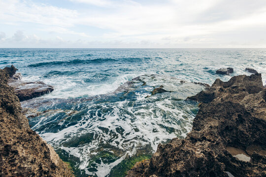 Rugged coastline with waves crashing against dark rocks under a cloudy sky. Ambon island, Maluku Islands, Indonesia