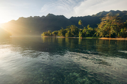 Serene tropical landscape with lush mountains and calm clear water at sunrise. Saleman Village, Seram Island, Maluku, Indonesia
