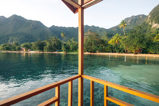 A serene mountain view from a waterside balcony with clear turquoise water and lush greenery. Saleman Village, Seram Island, Maluku, Indonesia
