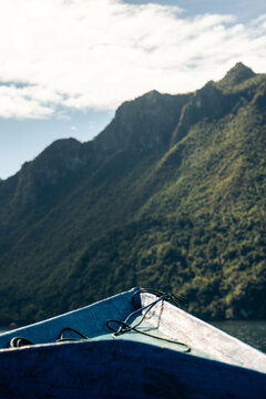 Blue boat prow points towards lush green mountain under a partly cloudy sky. Saleman Village, Seram Island, Maluku, Indonesia