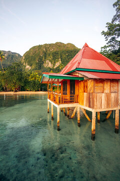A wooden hut on stilts over clear water with a mountain and trees in the background. Saleman Village, Seram Island, Maluku, Indonesia
