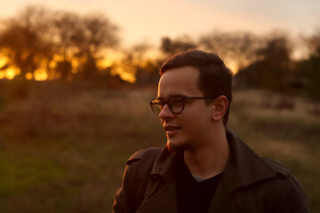 Young man with glasses smiling at sunset in a park. Perfect for lifestyle, happiness, and outdoor portrait stock content. A relaxed portrait of a young man 25 years wearing glasses smiling outside