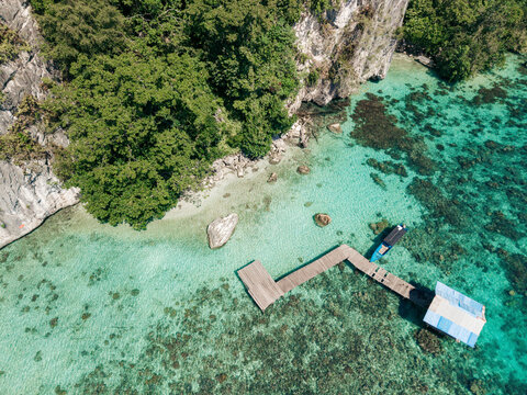 Aerial view of a wooden dock extending over clear turquoise water near lush green foliage. Saleman Village, Seram Island, Indonesia