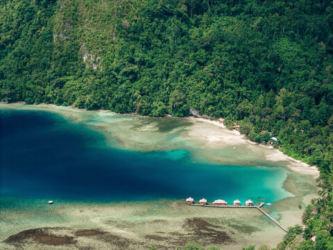 Aerial view of a lush green jungle coastline with turquoise waters and overwater bungalows. Saleman Village, Seram Island, Indonesia