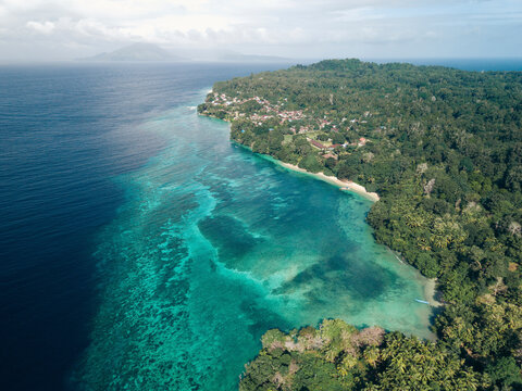 Aerial view of lush tropical coastline with vibrant blue and turquoise ocean waters. Pulau Ai or Ai Island, Banda, Central Maluku Regency, Maluku, Indonesia
