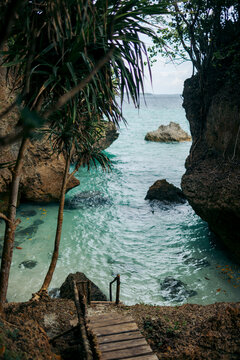 Rocky coastal path leading to turquoise sea through lush vegetation. Tanjung Vat La Roa, Kei Kecil, Southeast Maluku, Indonesia