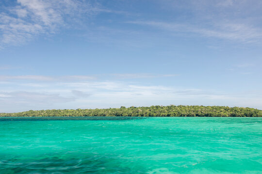 Vibrant turquoise sea with a dense green island under a clear blue sky. Pulau Bair or Bair Island in Kei Kecil, Southeast Maluku Regency, Maluku, Indonesia