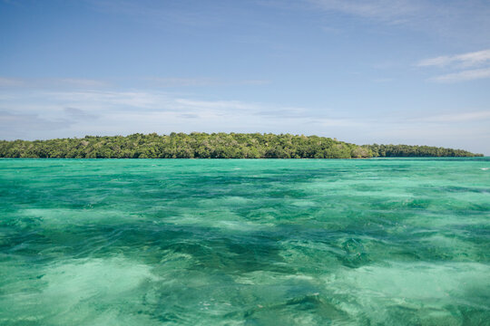 Tropical island with lush green forest surrounded by clear turquoise ocean under blue skies. Pulau Bair or Bair Island in Kei Kecil, Southeast Maluku Regency, Maluku, Indonesia