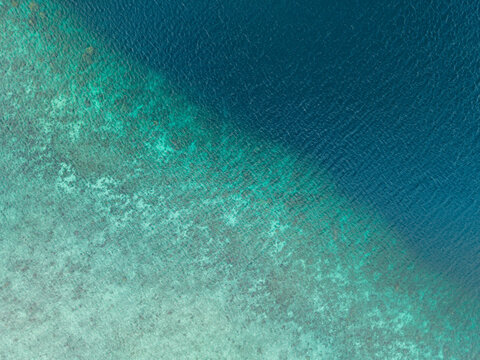 Aerial view of a deep blue ocean meeting a light sandy seabed along a diagonal line. Pantai Ngurbloat or Ngurbloat Beach in Kei Kecil, Southeast Maluku, Indonesia