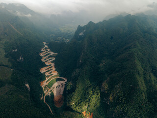 Aerial view of a winding road cutting through lush green mountains under a cloudy sky. Khau Coc Cha Mountain Pass, Bao Lac, Cao Bang, Vietnam