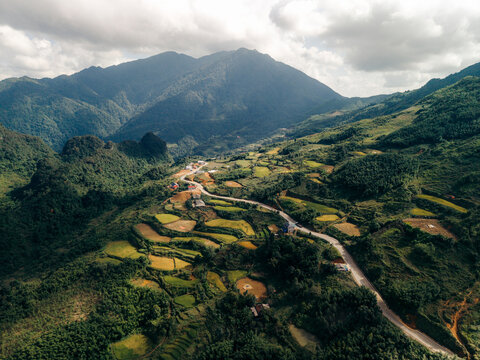 Aerial view of lush green valleys with winding roads and mountain backdrop under a cloudy sky. Nguyen B&Iuml;nh District, Cao Bang, Vietnam