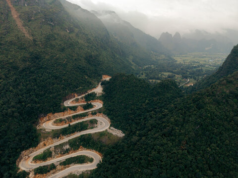 Aerial view of winding mountain road surrounded by lush green forest and misty peaks. Khau Coc Cha Mountain Pass, Bao Lac, Cao Bang, Vietnam