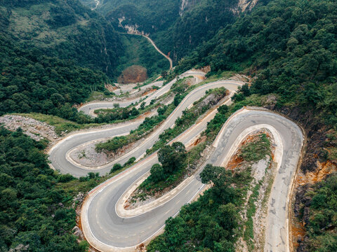 Aerial view of a winding mountain road surrounded by lush green forests and steep hills. Khau Coc Cha Mountain Pass, Bao Lac, Cao Bang, Vietnam