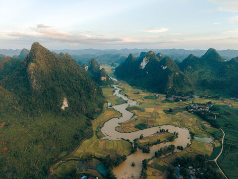 Aerial view of lush green fields, winding river, and mountains under a cloudy sky. Phong Nam, Tr˘ng Kh&middot;nh District, Cao Bang, Vietnam