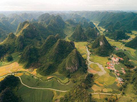 Aerial view of lush green mountains and patchwork fields with a small village below. Phong Nam, Tr˘ng Kh&middot;nh District, Cao Bang, Vietnam