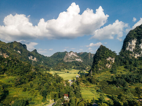 Lush green valley surrounded by rugged mountains under a blue sky with fluffy clouds.   Tr˘ng Kh&middot;nh District, Cao Bang, Vietnam