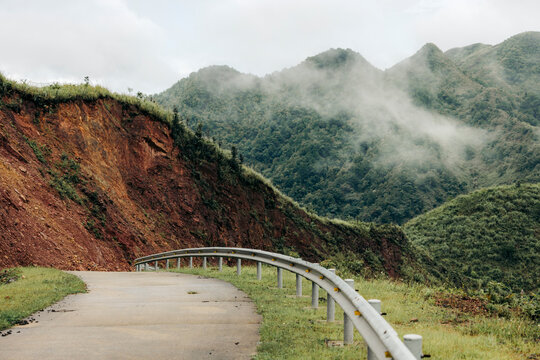 Misty mountain road winding through lush green hills with visible erosion on the roadside. Binh Lieu District, Quang Ninh, Vietnam
