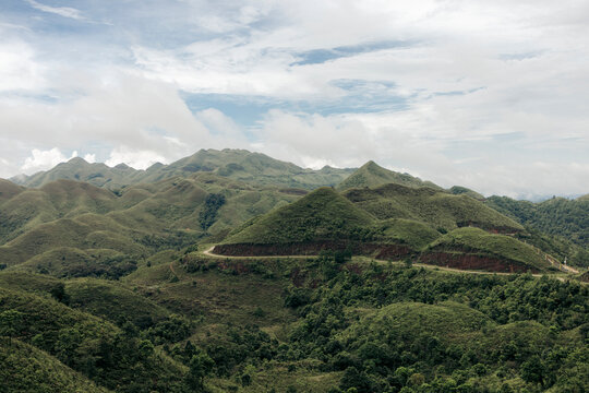 Rolling green hills under a cloudy blue sky with a winding road through the landscape. Binh Lieu District, Quang Ninh, Vietnam