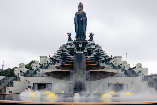 Large statue atop a multi-tiered structure with fog and yellow lotus flowers in foreground. Black Virgin Mountain, Tay Ninh, Vietnam