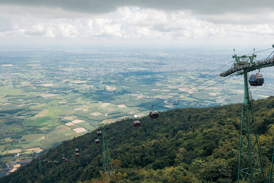 Cable cars traverse above lush green hills with a vast landscape under cloudy skies. Black Virgin Mountain, Tay Ninh, Vietnam