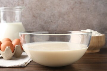 Liquid dough in bowl and ingredients on wooden table, closeup