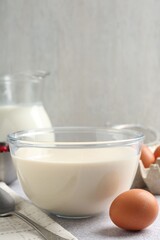 Liquid dough in bowl and ingredients on light grey table, closeup