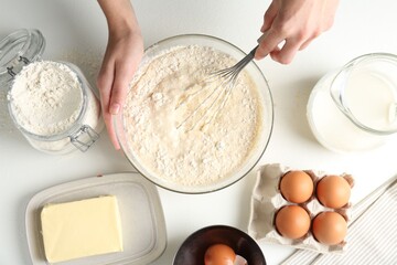 Woman making batter (liquid dough) at white table, top view