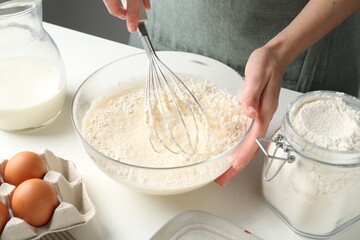 Woman making batter (liquid dough) at white table indoors, closeup