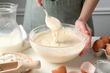Woman making batter (liquid dough) at white table indoors, closeup