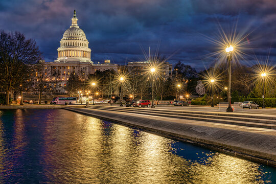 Illuminated US Capitol at dusk with reflections on the calm water. Washington DC, WA, USA