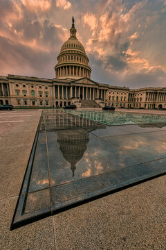 United States Capitol building with dramatic sunset and reflection in foreground glass. Washington DC, WA, USA