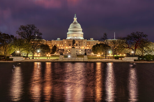 The United States Capitol illuminated at night with a reflection in the foreground water. Washington DC, WA, USA
