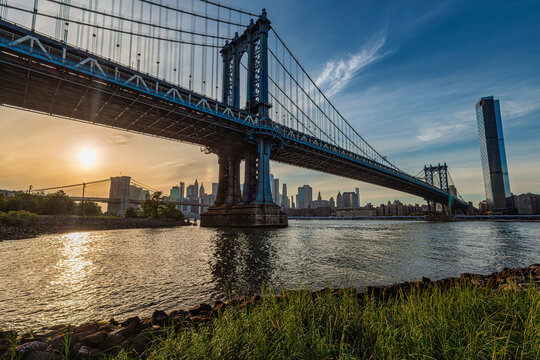 Sunrise over a large suspension bridge with city skyline in the background. New York City, NY, USA Williamsburg Bridge over East River